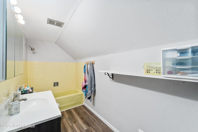 bathroom with vaulted ceiling, a textured ceiling, vanity, hardwood / wood-style flooring, and a washtub