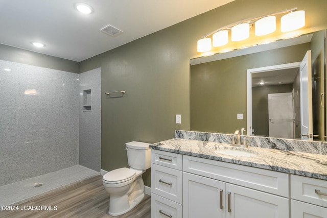 bathroom with hardwood / wood-style floors, vanity, toilet, and a tile shower