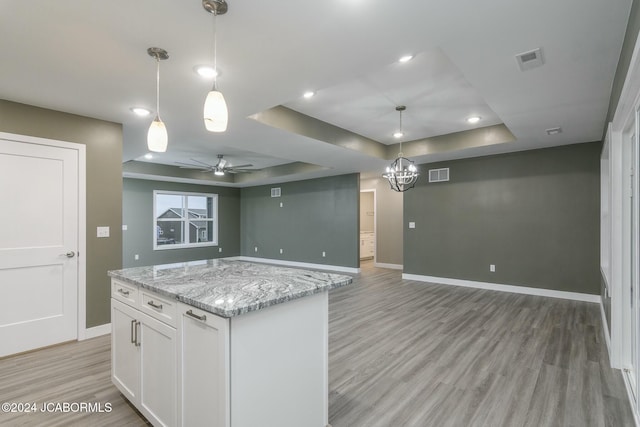 kitchen with hanging light fixtures, light stone counters, light hardwood / wood-style floors, a tray ceiling, and white cabinets