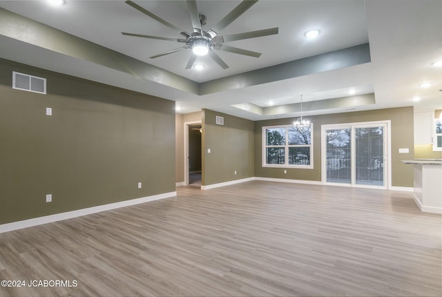 interior space with a tray ceiling, light hardwood / wood-style floors, and ceiling fan with notable chandelier