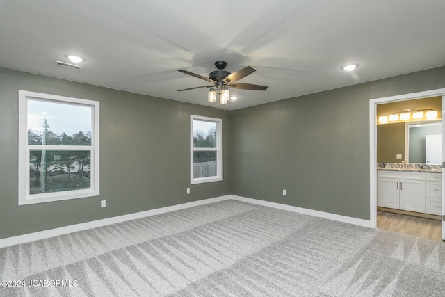 unfurnished bedroom with connected bathroom, ceiling fan, light carpet, and multiple windows