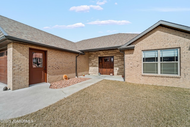 doorway to property featuring brick siding and a shingled roof