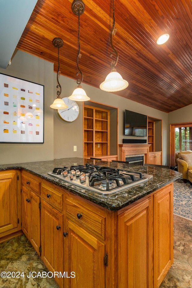 kitchen with hanging light fixtures, stainless steel gas stovetop, fridge, dark stone counters, and built in features