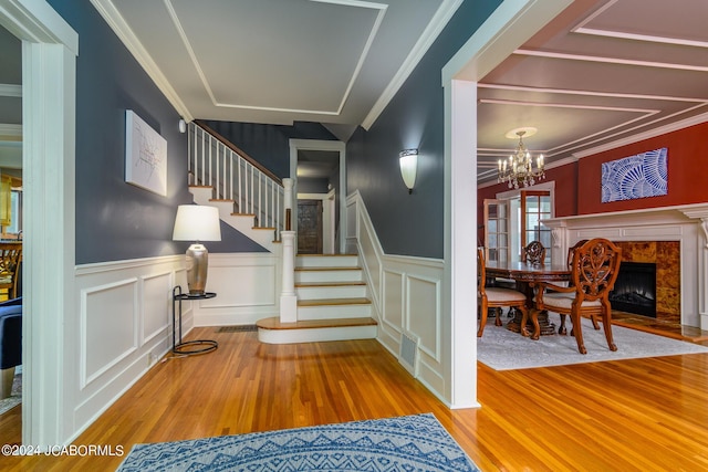 staircase with a high end fireplace, wood-type flooring, ornamental molding, and a notable chandelier