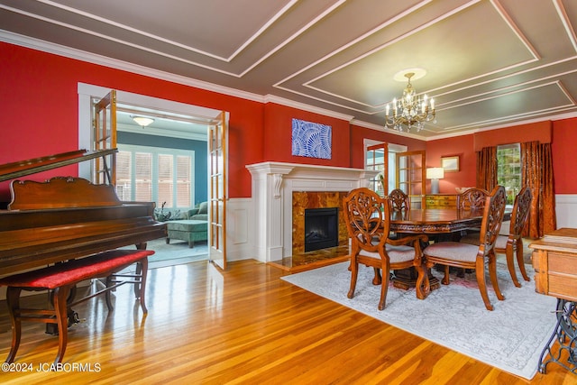 dining space with a fireplace, french doors, ornamental molding, wood-type flooring, and a notable chandelier