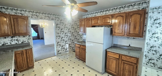 kitchen with ceiling fan with notable chandelier, light floors, brown cabinets, and freestanding refrigerator