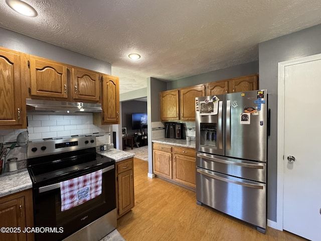 128 Don Dr, Linn, MO 65051 - kitchen with stainless steel appliances, under cabinet range hood, light wood finished floors, decorative backsplash, and a textured ceiling