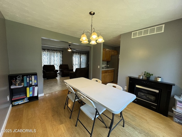 128 Don Dr, Linn, MO 65051 - dining space featuring light wood-style floors, a chandelier, a textured ceiling, a glass covered fireplace, and ceiling fan