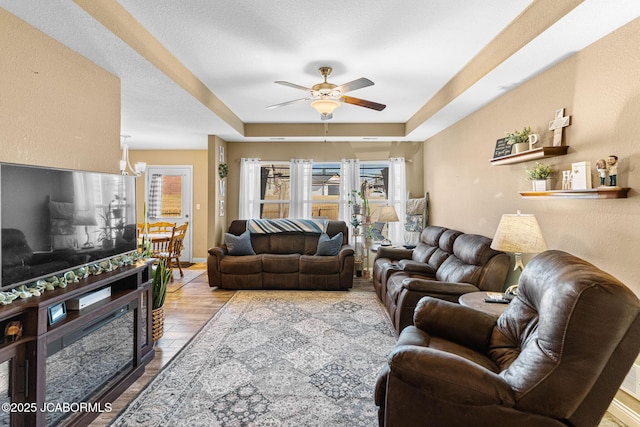 living area featuring ceiling fan, a tray ceiling, baseboards, and wood finished floors