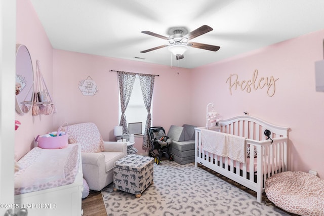 bedroom with visible vents, a crib, a ceiling fan, and light wood finished floors