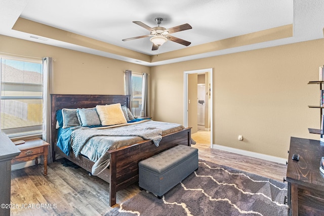 bedroom featuring visible vents, multiple windows, a tray ceiling, and wood finished floors