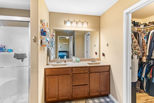 bathroom with double vanity, a spacious closet, a shower stall, and a sink