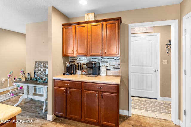 kitchen featuring light wood finished floors, tasteful backsplash, baseboards, light countertops, and brown cabinets