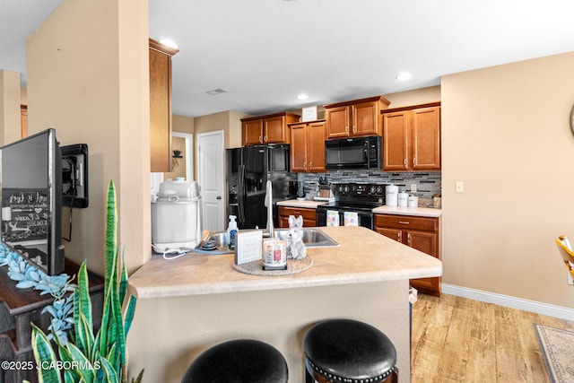 kitchen featuring black appliances, backsplash, a peninsula, brown cabinetry, and light wood finished floors