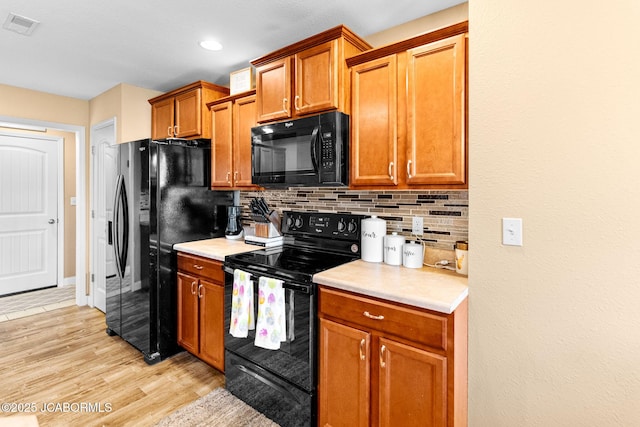 kitchen with light wood-type flooring, tasteful backsplash, black appliances, and light countertops