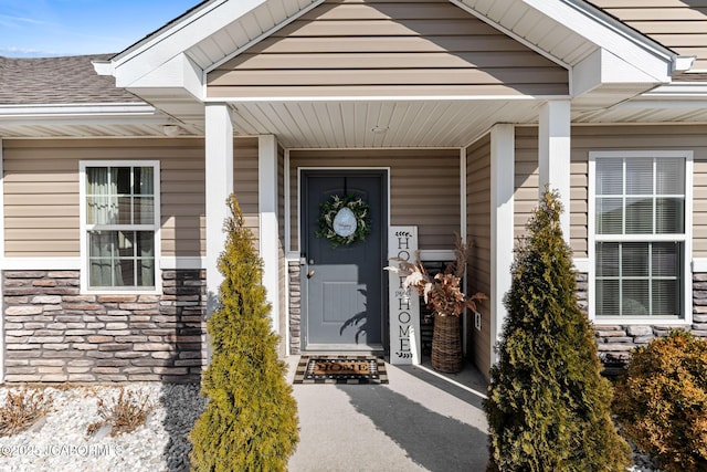 entrance to property featuring stone siding and a shingled roof