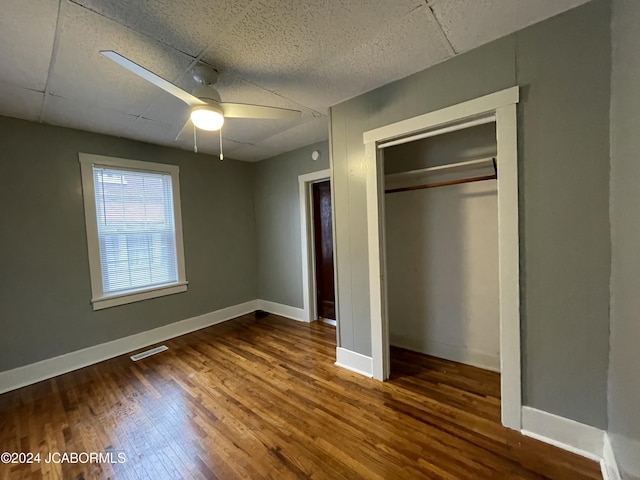 unfurnished bedroom with a paneled ceiling, a closet, ceiling fan, and dark wood-type flooring