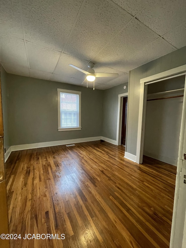 unfurnished bedroom featuring wood-type flooring, a closet, a drop ceiling, and ceiling fan