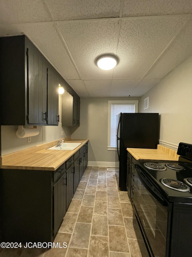 kitchen featuring a drop ceiling, sink, black appliances, light tile patterned floors, and butcher block counters