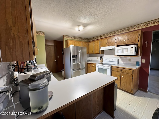 kitchen with white appliances, a peninsula, light countertops, under cabinet range hood, and brown cabinets