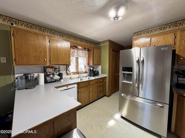 kitchen featuring brown cabinets, stainless steel refrigerator with ice dispenser, a sink, light floors, and dishwasher