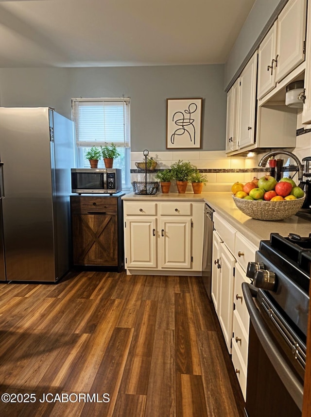 kitchen with tasteful backsplash, dark wood-style floors, light countertops, white cabinets, and appliances with stainless steel finishes