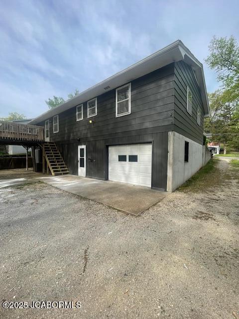 rear view of house featuring an attached garage, stairway, a deck, and dirt driveway