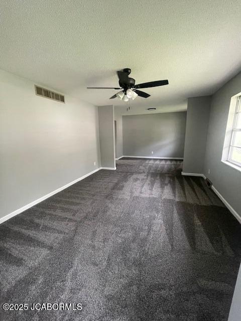 unfurnished room featuring a textured ceiling, ceiling fan, baseboards, dark colored carpet, and visible vents