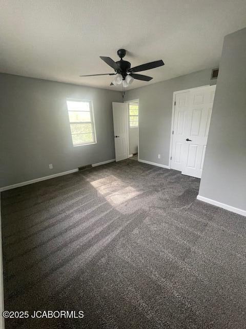 unfurnished bedroom with dark carpet, visible vents, a ceiling fan, and baseboards