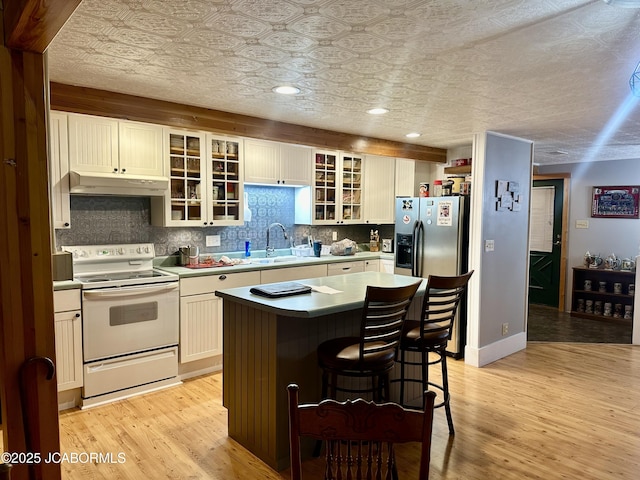 11 Copperhead Rd, Eldon, MO 65026 - kitchen featuring white electric stove, under cabinet range hood, backsplash, a center island, and light wood-style flooring
