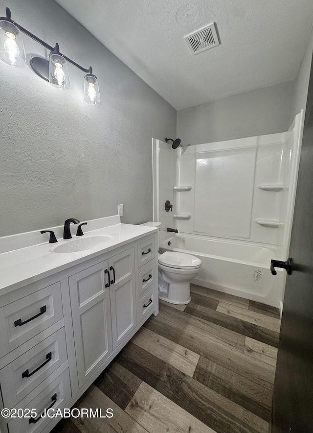 full bathroom with toilet, wood-type flooring,  shower combination, a textured ceiling, and vanity