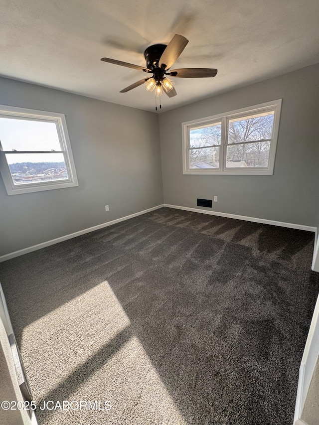 empty room featuring ceiling fan and dark colored carpet