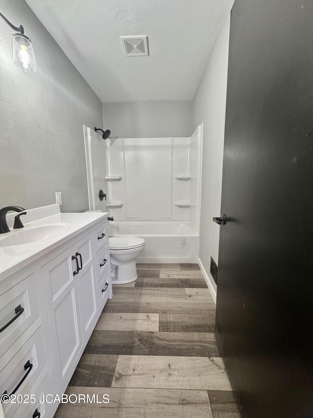 full bathroom with hardwood / wood-style floors, washtub / shower combination, vanity, toilet, and a textured ceiling