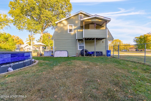 rear view of house featuring a balcony, a covered pool, and a lawn