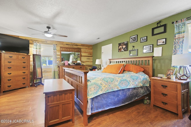 bedroom featuring hardwood / wood-style floors, ceiling fan, a textured ceiling, and wooden walls