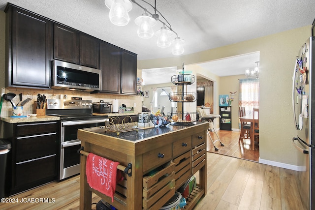 kitchen featuring appliances with stainless steel finishes, light wood-type flooring, backsplash, dark brown cabinets, and a notable chandelier