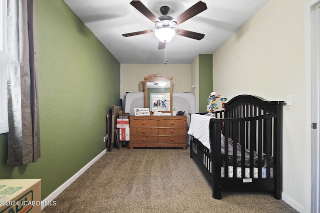 bedroom featuring a crib, a textured ceiling, carpet floors, and ceiling fan