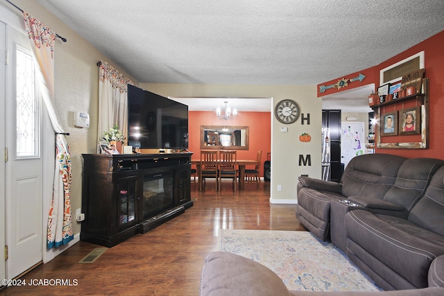 living room with a textured ceiling, dark wood-type flooring, and an inviting chandelier