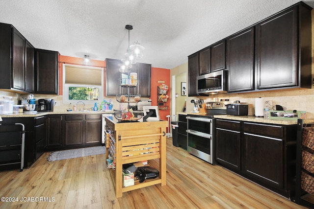 kitchen with dark brown cabinets, stainless steel appliances, sink, pendant lighting, and light hardwood / wood-style floors