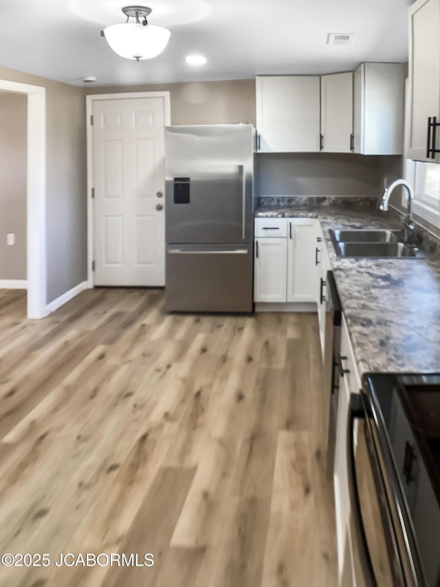 kitchen featuring visible vents, light wood-style flooring, freestanding refrigerator, a sink, and baseboards