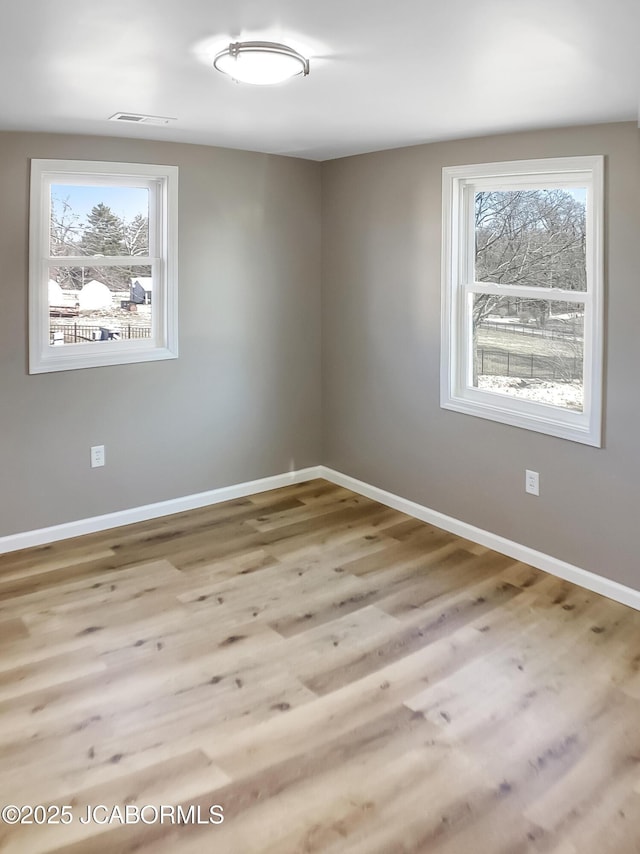 empty room with a wealth of natural light, wood finished floors, and visible vents