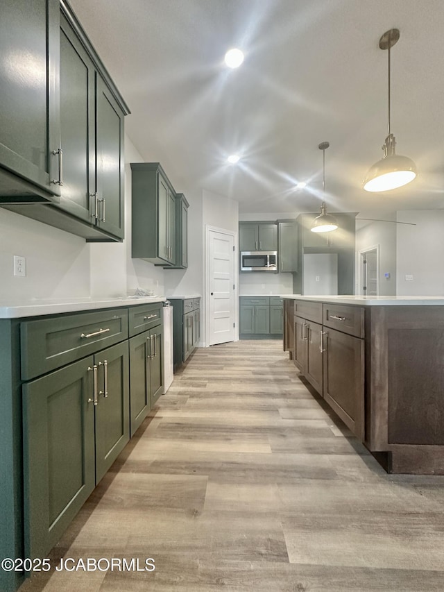 kitchen featuring decorative light fixtures, light countertops, stainless steel microwave, light wood-style flooring, and green cabinetry