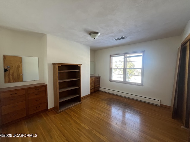 unfurnished bedroom with wood-type flooring and baseboard heating