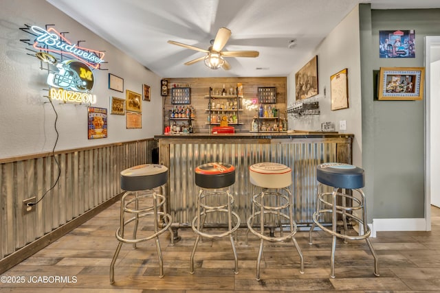 bar with ceiling fan, wood walls, bar area, and wood finished floors