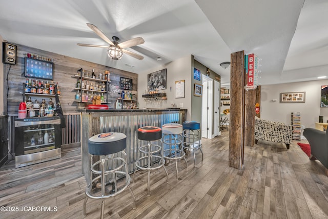 bar with beverage cooler, ceiling fan, bar area, and wood finished floors