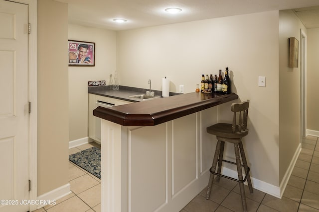 bar with indoor wet bar, light tile patterned floors, baseboards, and a sink