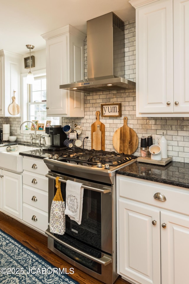 kitchen featuring white cabinets, stainless steel gas range oven, wall chimney exhaust hood, and backsplash