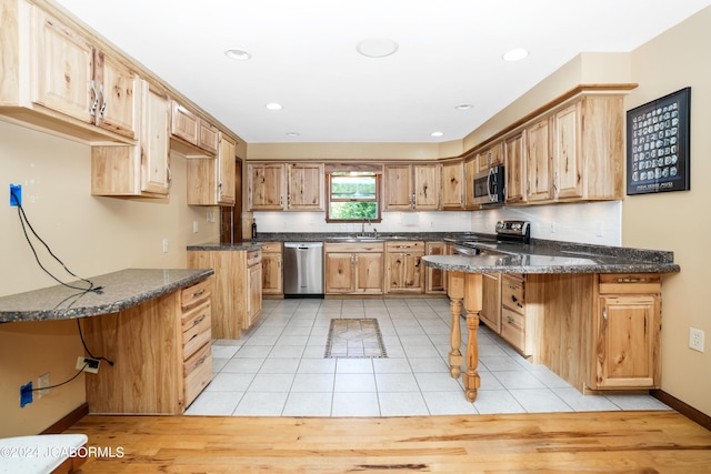 kitchen featuring sink, stainless steel appliances, kitchen peninsula, dark stone counters, and light tile patterned floors