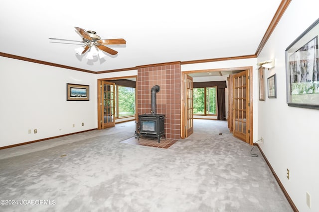 unfurnished living room featuring light carpet, a wealth of natural light, a wood stove, and ceiling fan