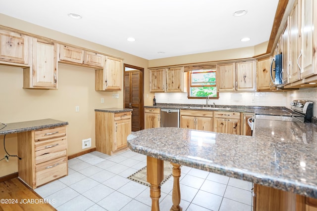 kitchen featuring kitchen peninsula, a breakfast bar, stainless steel appliances, sink, and dark stone countertops